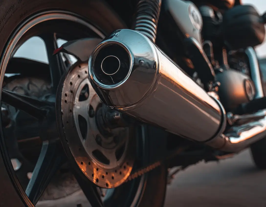 Nahaufnahme eines glänzenden Motorrad-Auspuffs am Hinterrad mit Bremsscheibe